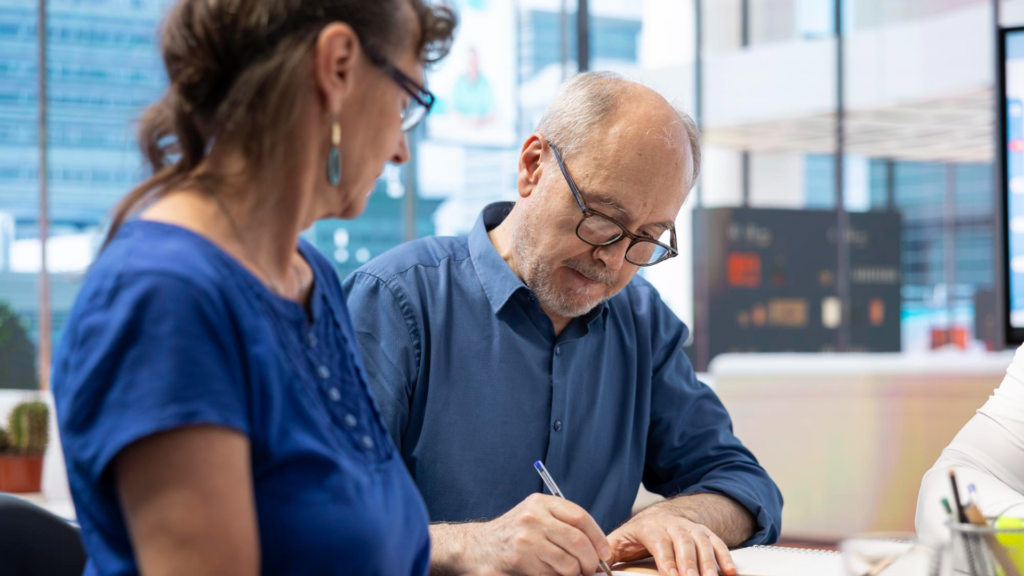 older man signing a document while a woman sits beside him